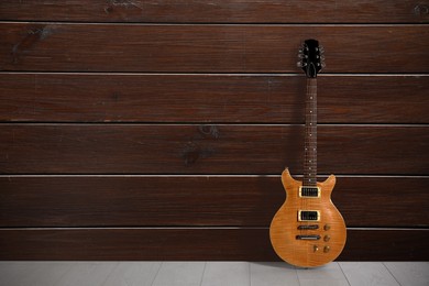 Image of Modern electric guitar on floor near wooden wall. Space for text