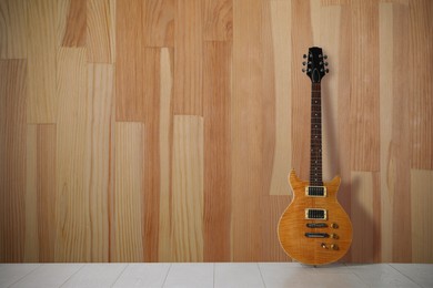 Image of Modern electric guitar on floor near wooden wall. Space for text