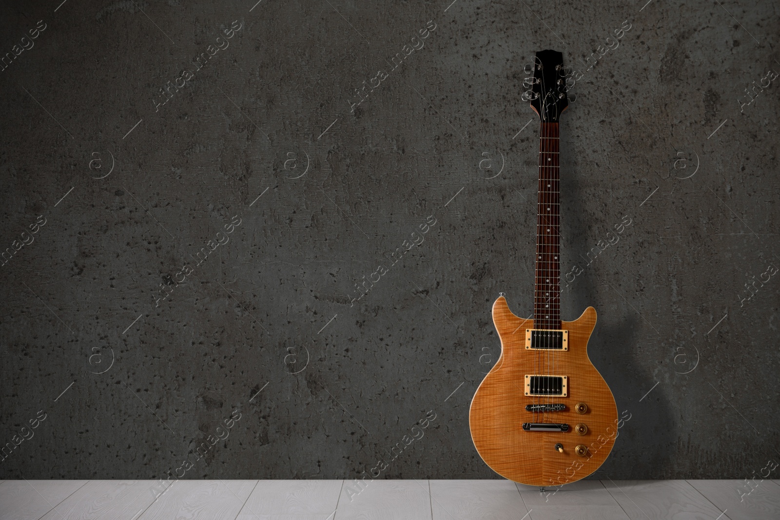 Image of Modern electric guitar on floor near grey grunge wall. Space for text