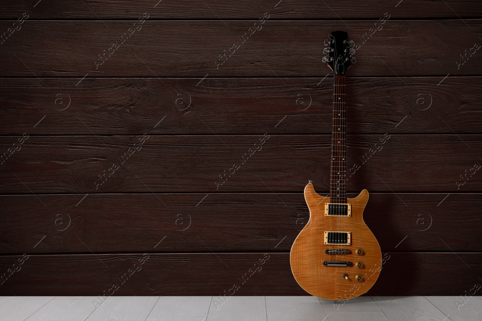 Image of Modern electric guitar on floor near wooden wall. Space for text