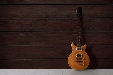 Image of Modern electric guitar on floor near wooden wall. Space for text