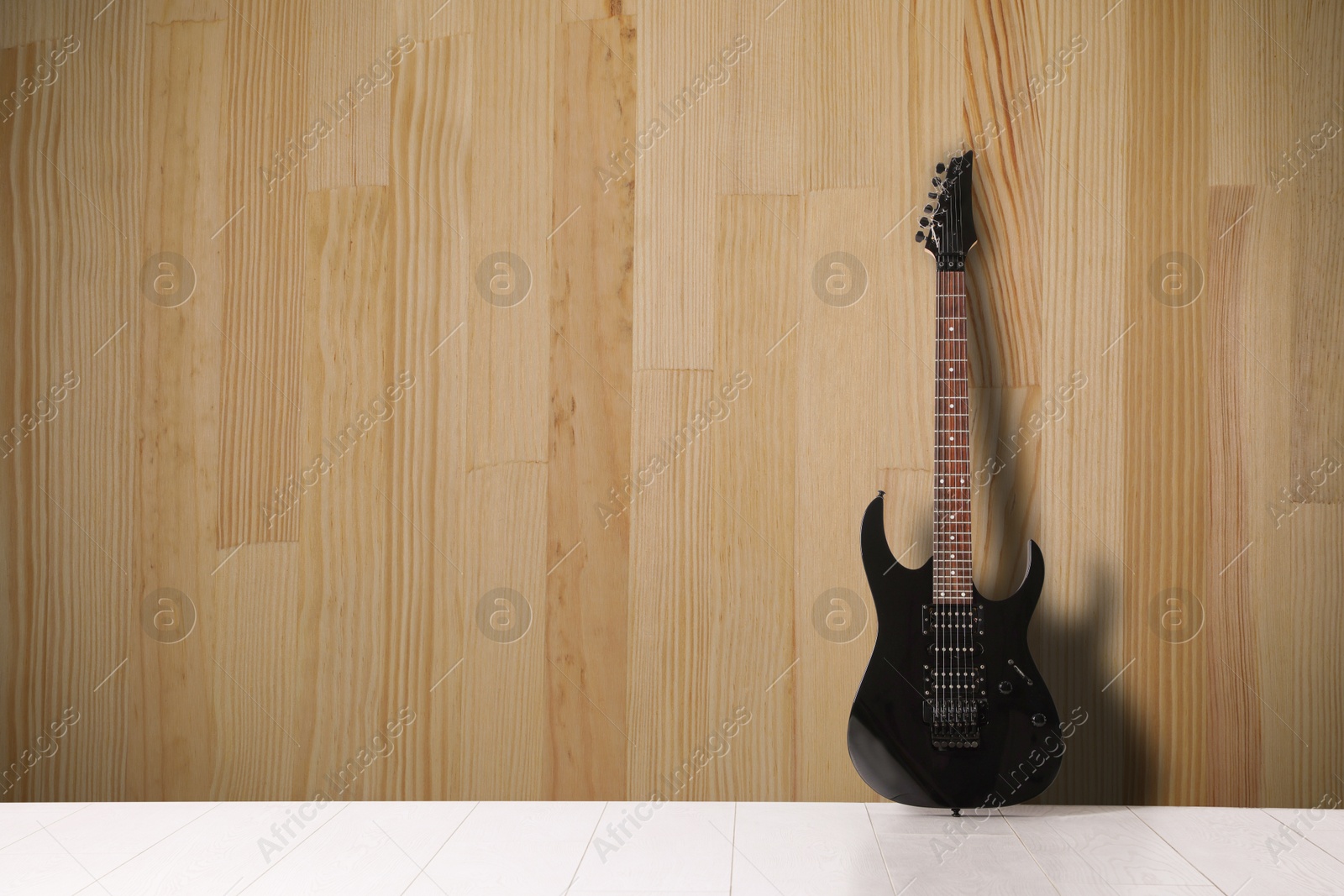 Image of Modern electric guitar on floor near wooden wall. Space for text