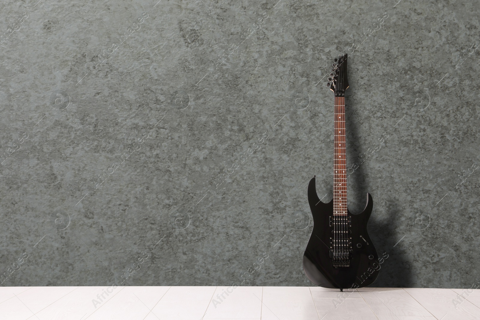 Image of Modern electric guitar on floor near grey grunge wall. Space for text