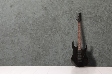 Image of Modern electric guitar on floor near grey grunge wall. Space for text