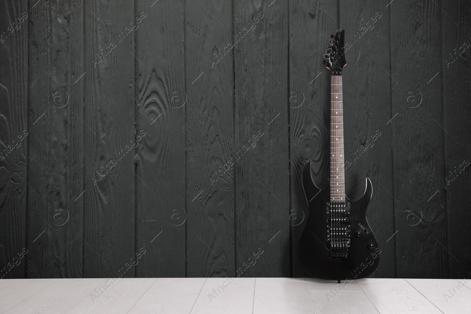 Image of Modern electric guitar near dark grey wooden wall. Space for text