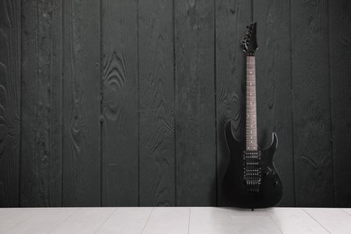 Image of Modern electric guitar near dark grey wooden wall. Space for text