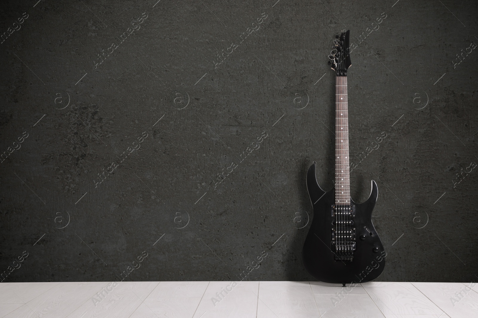 Image of Modern electric guitar on floor near dark grey grunge wall. Space for text