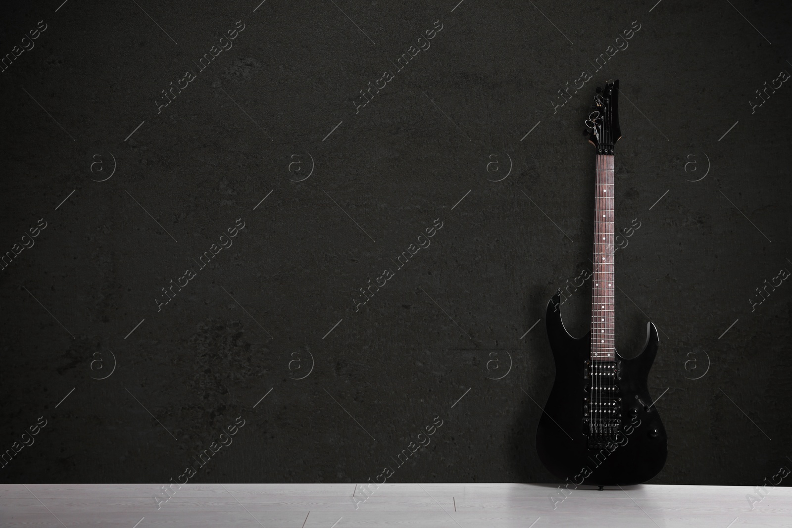 Image of Modern electric guitar on floor near black grunge wall. Space for text