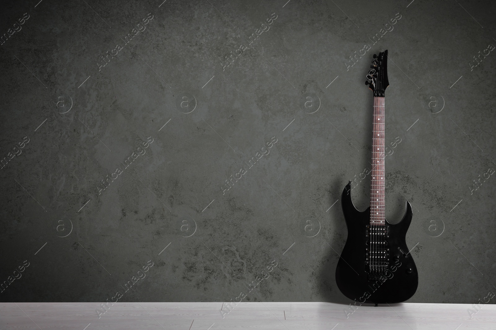 Image of Modern electric guitar on floor near grey grunge wall. Space for text