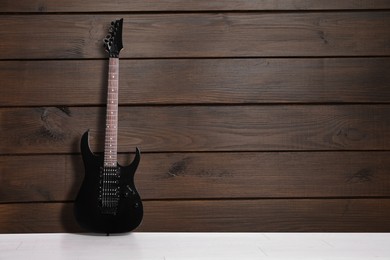 Image of Modern electric guitar on floor near wooden wall. Space for text