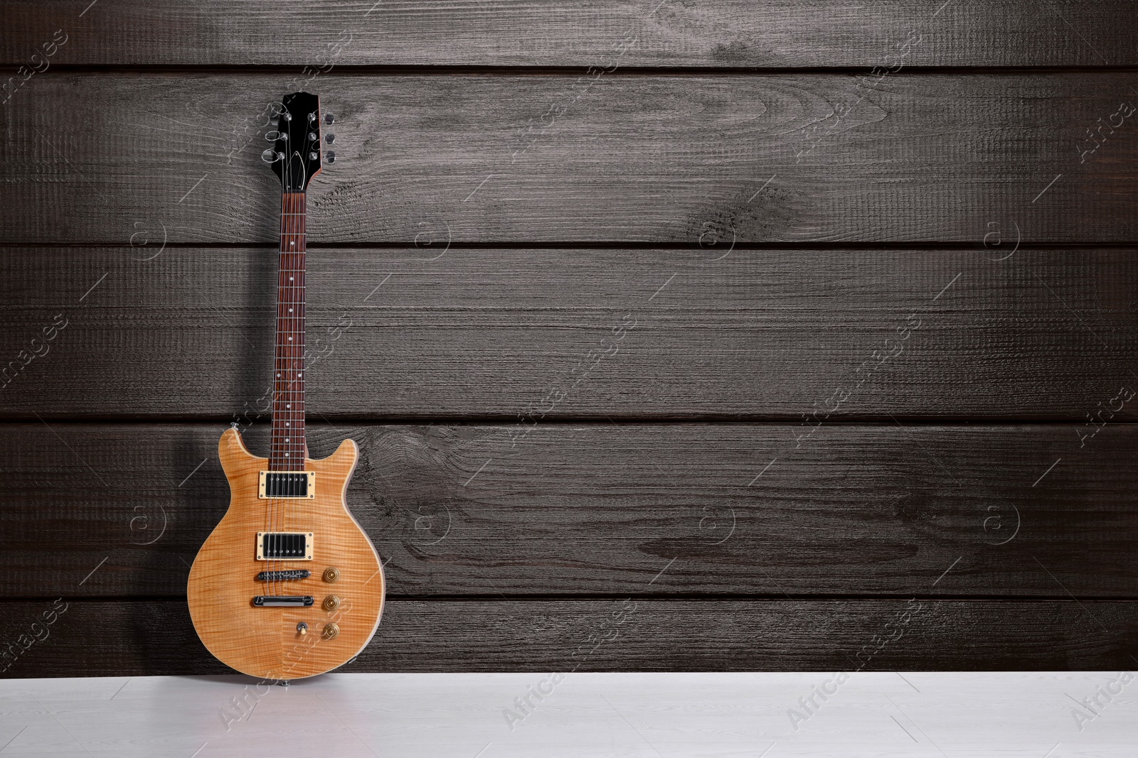 Image of Modern electric guitar on floor near wooden wall. Space for text