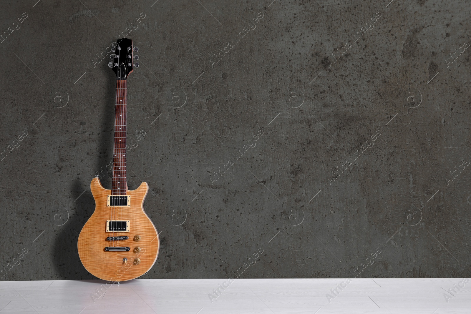 Image of Modern electric guitar on floor near grey grunge wall. Space for text