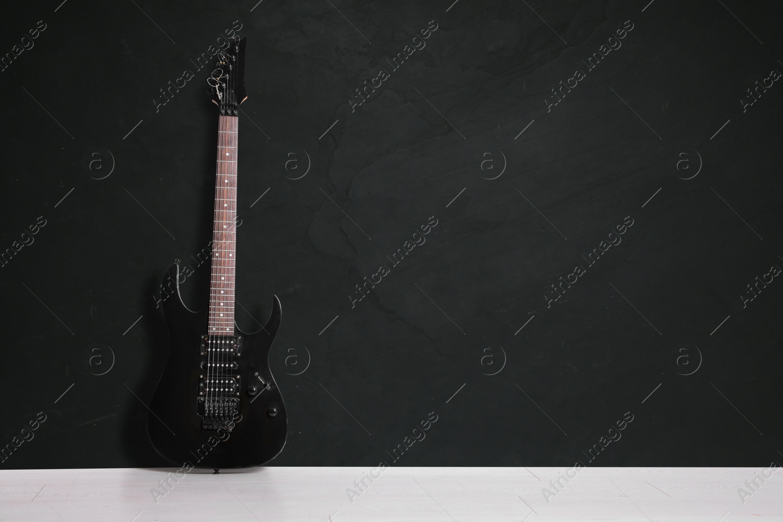 Image of Modern electric guitar on floor near black grunge wall. Space for text