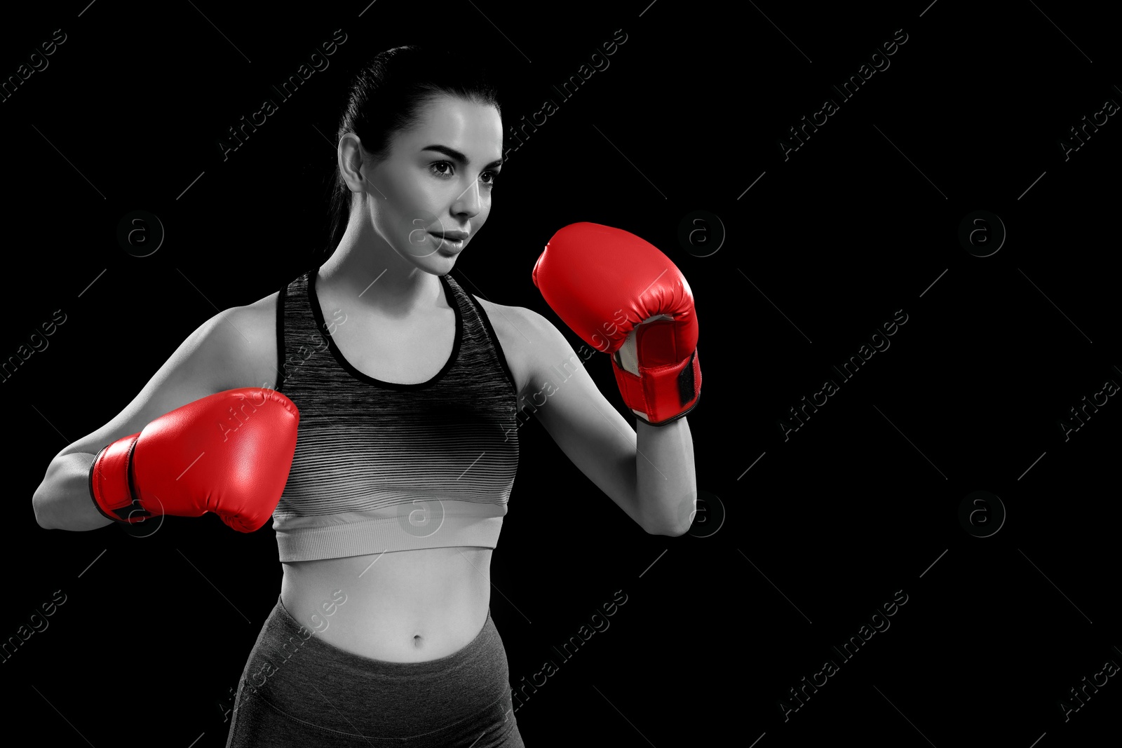 Image of Beautiful woman in boxing gloves training, black-and-white toning with color accent. Space for text