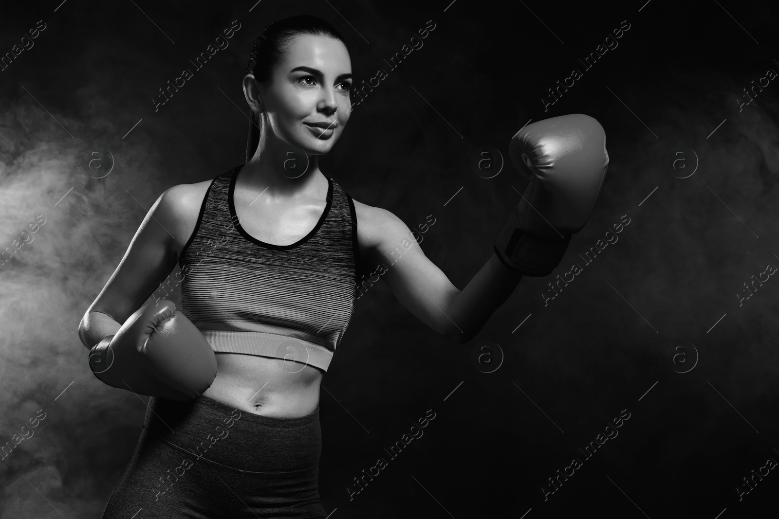 Image of Beautiful woman wearing boxing gloves training in smoke, black-and-white toning