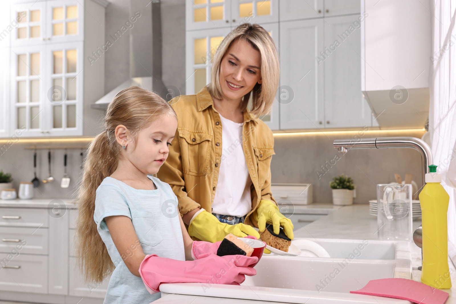 Photo of Happy housewife and her daughter washing dishes in kitchen together