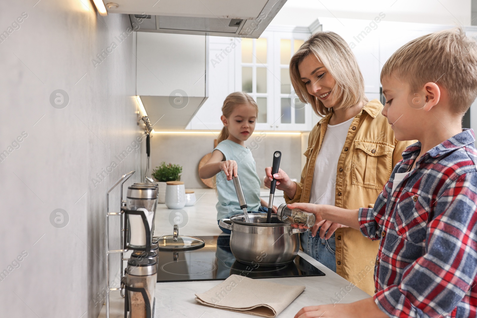 Photo of Happy housewife and her kids cooking together on stove in kitchen