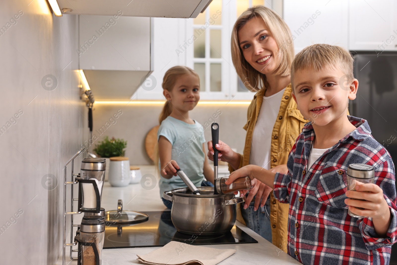 Photo of Happy housewife and her kids cooking together on stove in kitchen