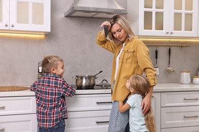 Photo of Tired housewife cooking on stove while her kids playing and distracting her in kitchen