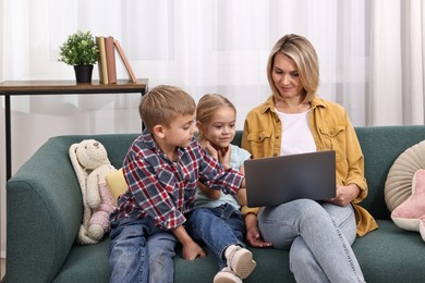 Housewife spending time with her kids and using laptop on couch at home