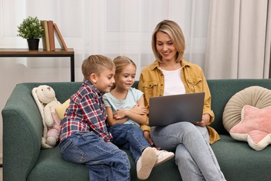 Housewife spending time with her kids and using laptop on couch at home