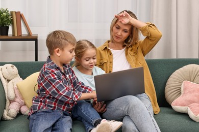 Photo of Tired housewife spending time with her kids and using laptop on couch at home