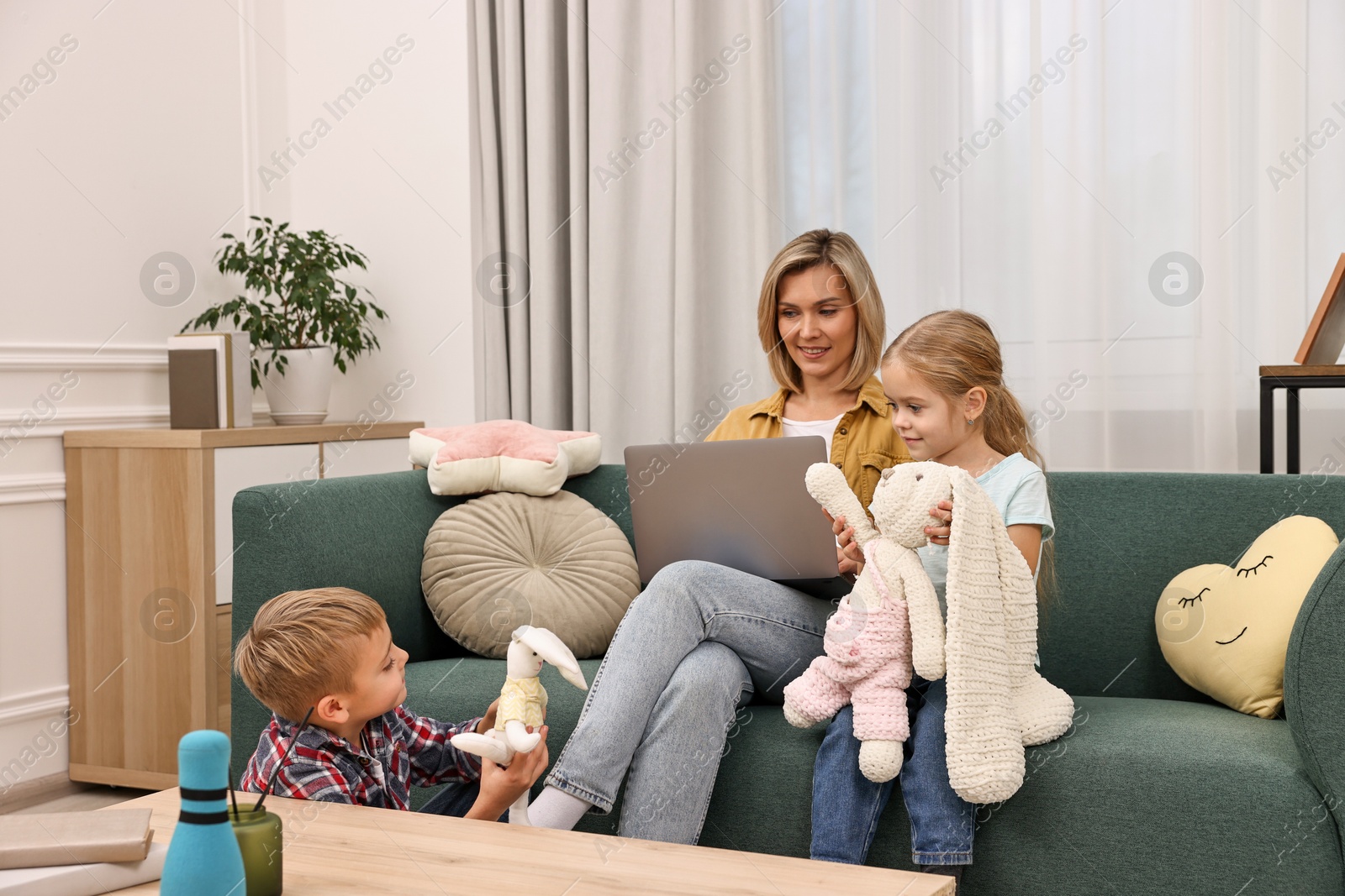 Photo of Housewife using laptop while her kids playing with toys at home