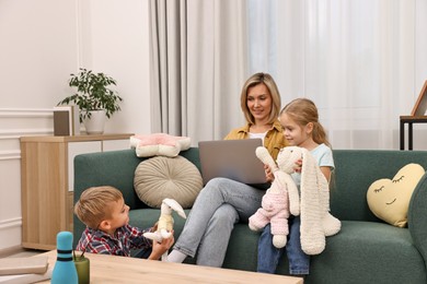 Housewife using laptop while her kids playing with toys at home