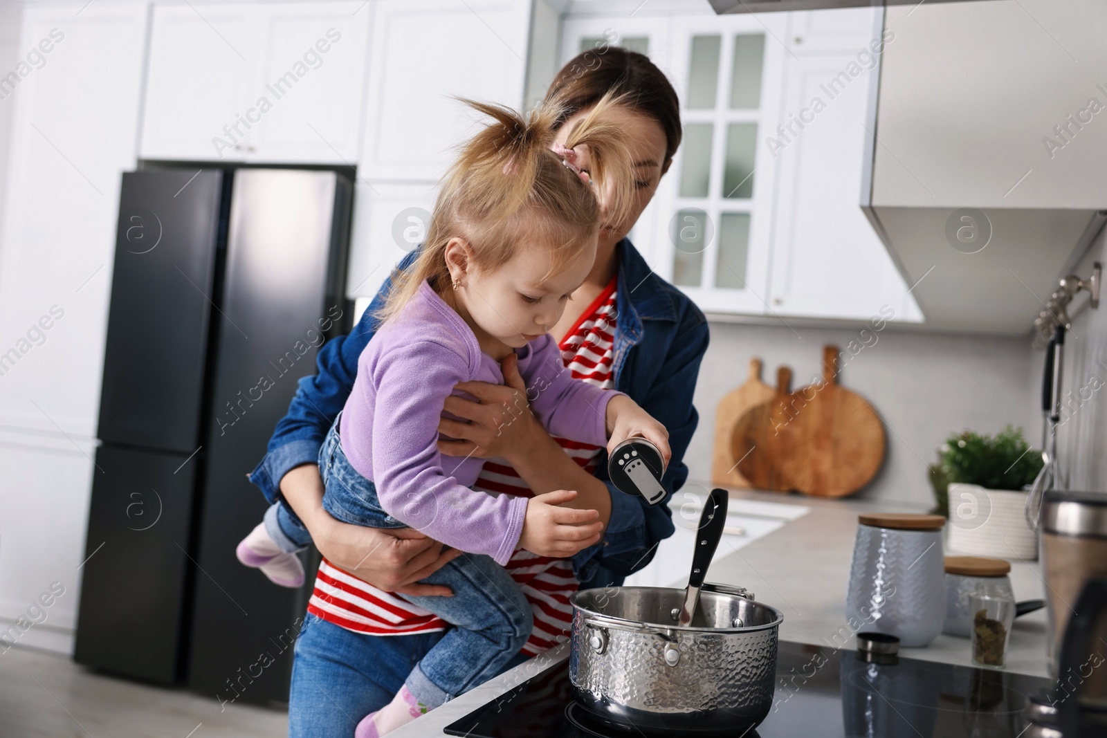 Photo of Busy housewife cooking with her little daughter in kitchen