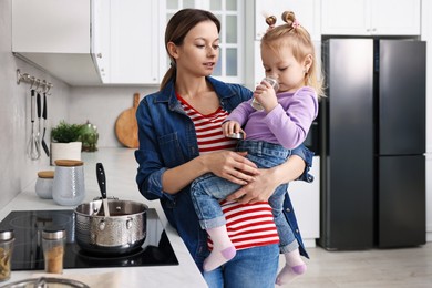 Busy housewife cooking with her little daughter in kitchen