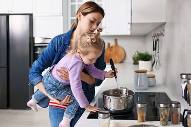 Photo of Busy housewife cooking with her little daughter in kitchen