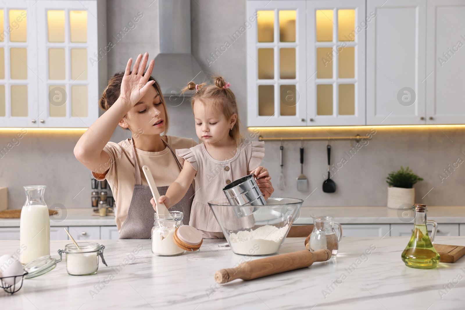 Photo of Tired housewife cooking with her little daughter at marble table in kitchen