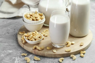 Photo of Glassware with fresh cashew milk and nuts on grey table, closeup