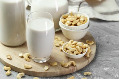 Photo of Glassware with fresh cashew milk and nuts on grey table, closeup