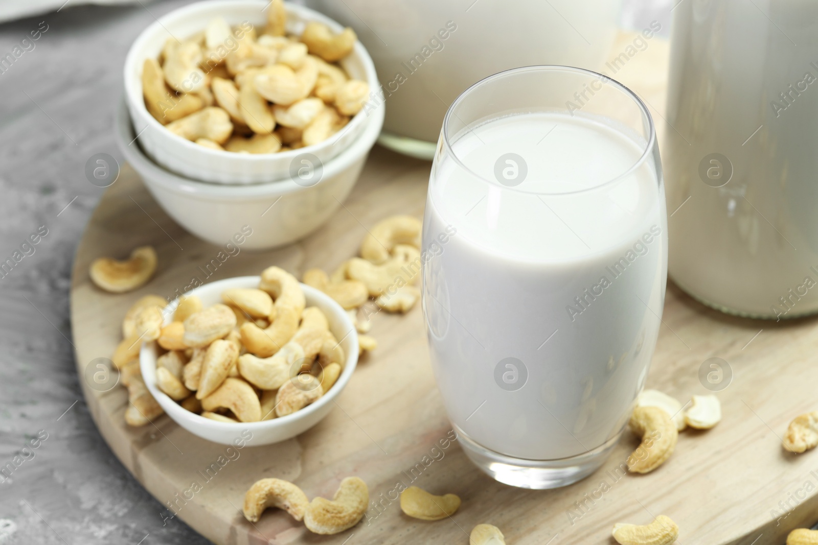 Photo of Fresh cashew milk in glass and nuts on grey table, closeup