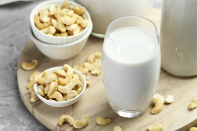 Fresh cashew milk in glass and nuts on grey table, closeup