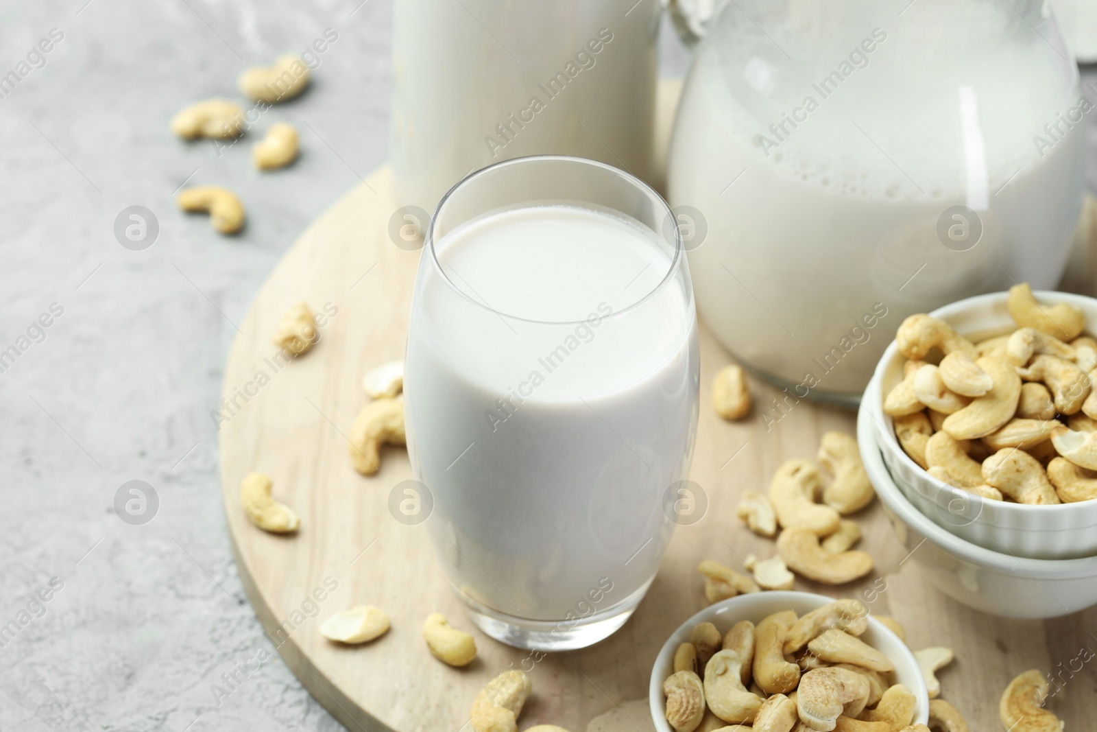 Photo of Fresh cashew milk in glass and nuts on grey table, closeup