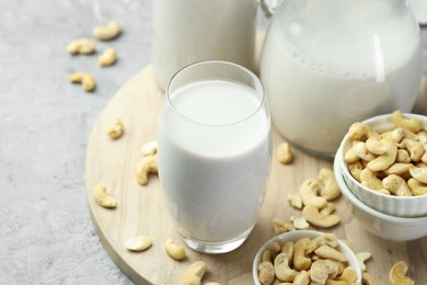 Fresh cashew milk in glass and nuts on grey table, closeup