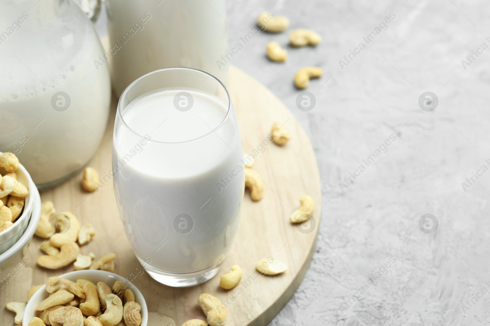 Photo of Fresh cashew milk in glass and nuts on grey table, closeup. Space for text