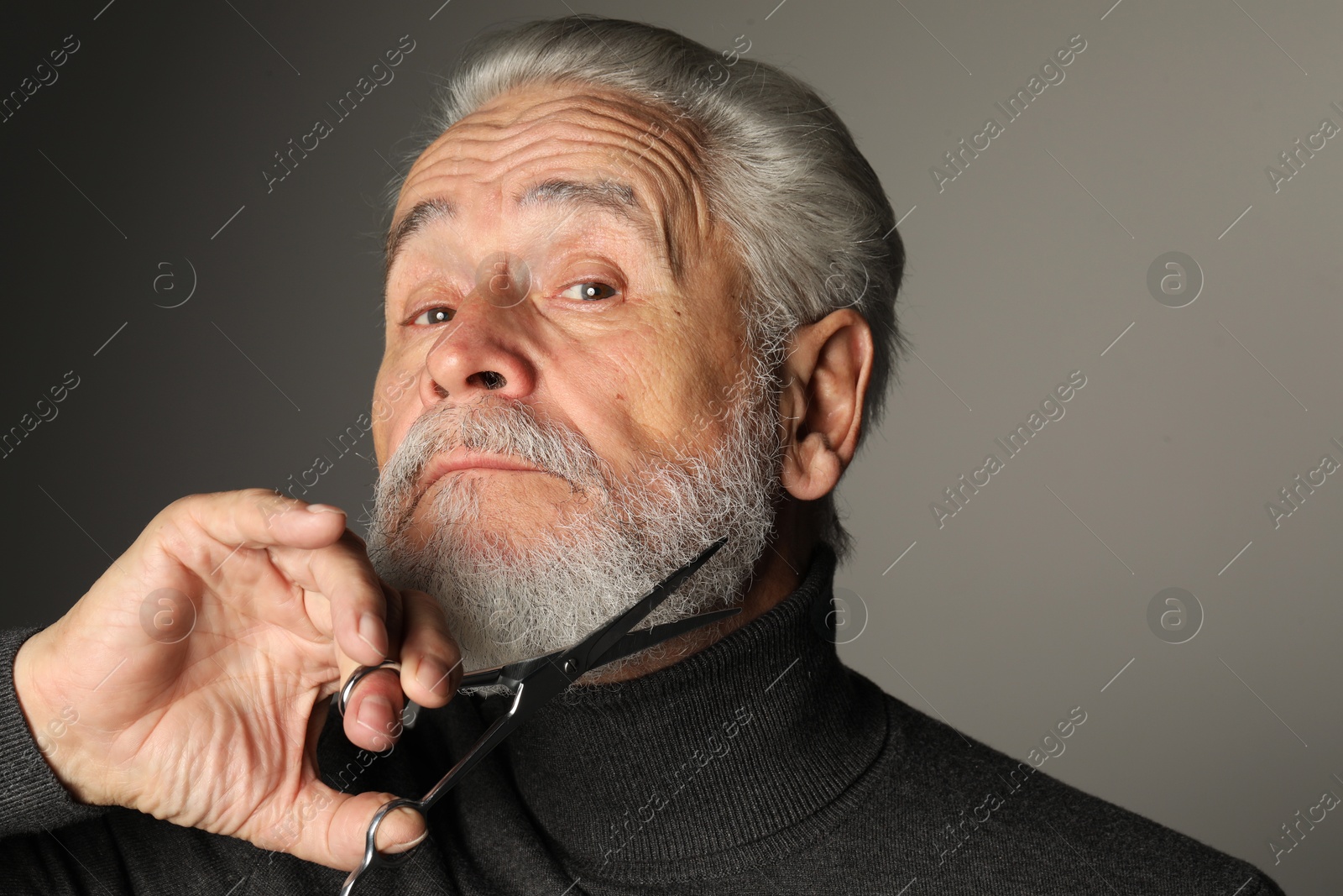 Photo of Senior man trimming beard with scissors on grey background