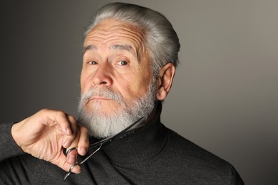 Photo of Senior man trimming beard with scissors on grey background