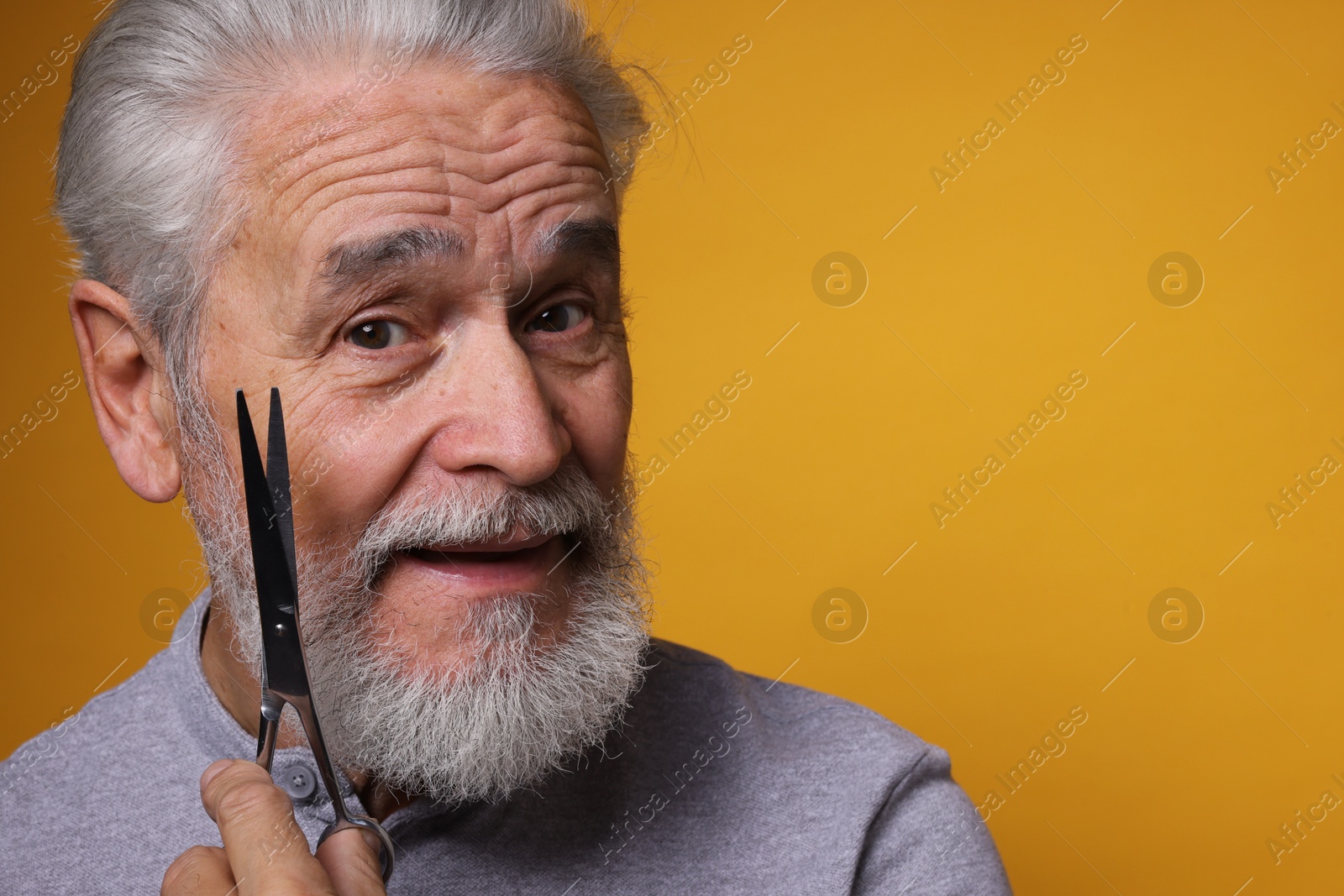 Photo of Bearded senior man holding scissors on orange background, space for text