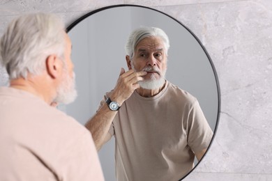 Photo of Bearded senior man near mirror in bathroom