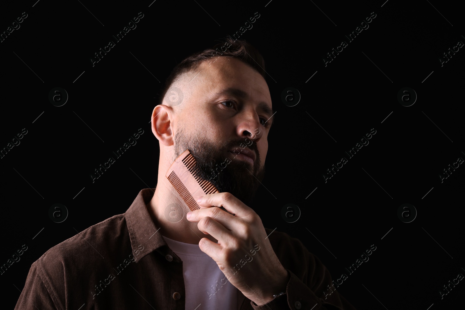 Photo of Handsome man combing beard on black background, space for text