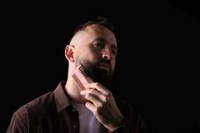 Photo of Handsome man combing beard on black background, space for text