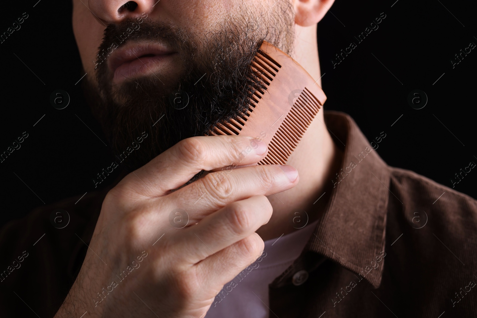 Photo of Man combing beard on black background, closeup