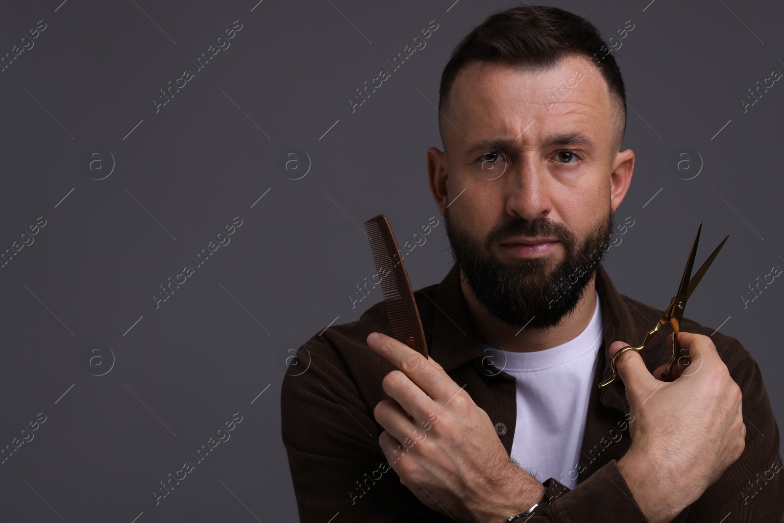 Photo of Bearded man holding comb and scissors on grey background, space for text