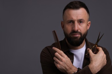 Photo of Bearded man holding comb and scissors on grey background, space for text