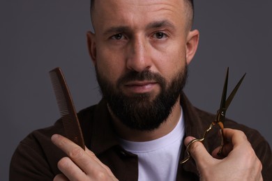 Photo of Bearded man holding comb and scissors on grey background