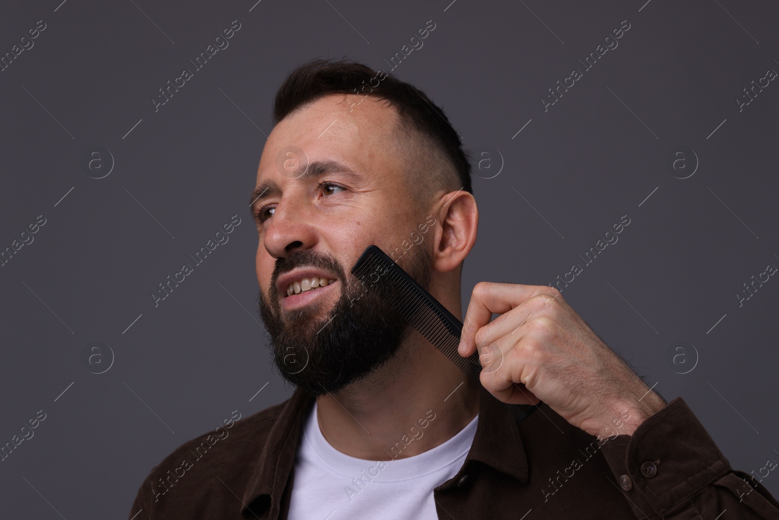 Photo of Handsome man combing beard on grey background